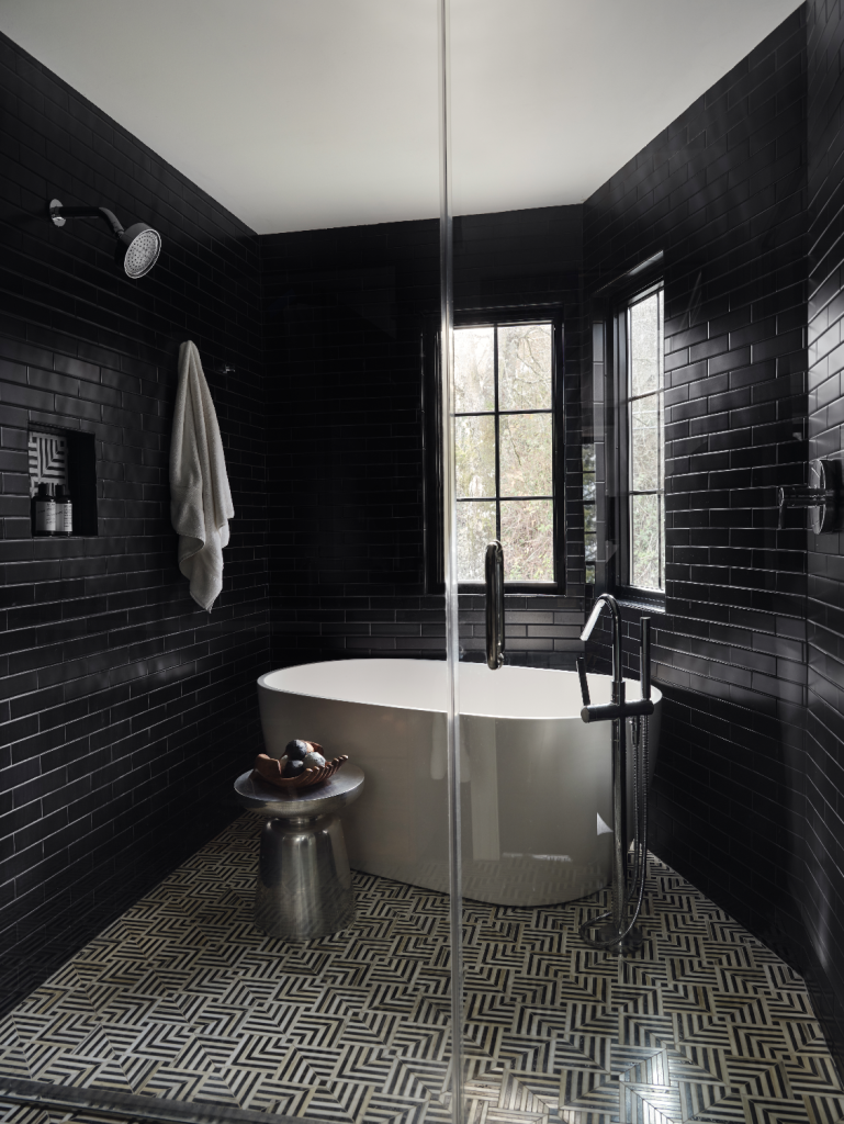 Luxury walk-in shower clad in glossy black tile with a freestanding soaking tub, geometric tile flooring, and black-framed windows.